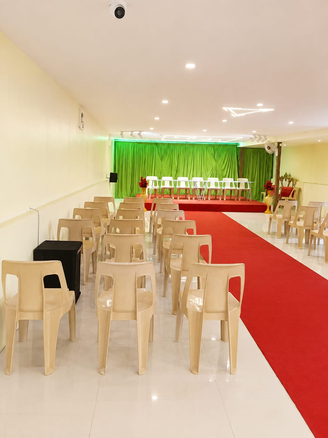 Event hall with red carpet aisle leading to a green draped stage
