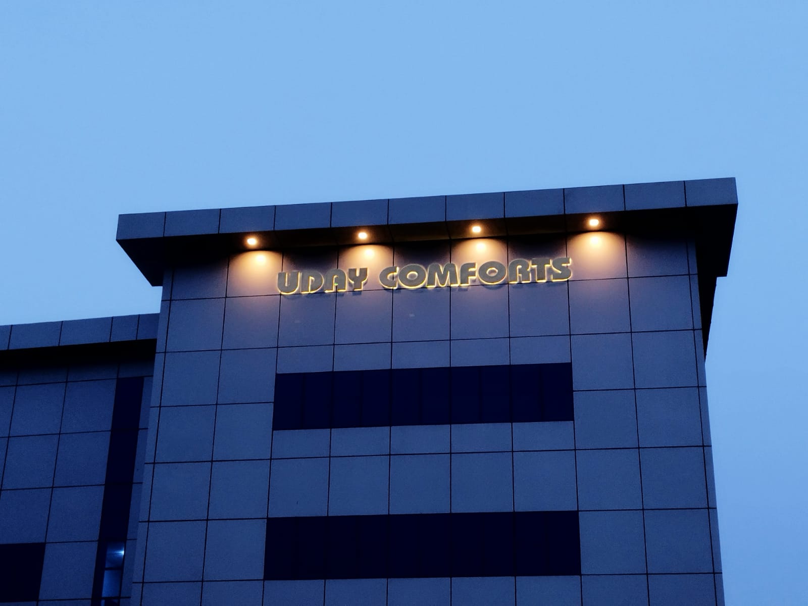 Illuminated Uday Comforts building sign at dusk in Kodlipet