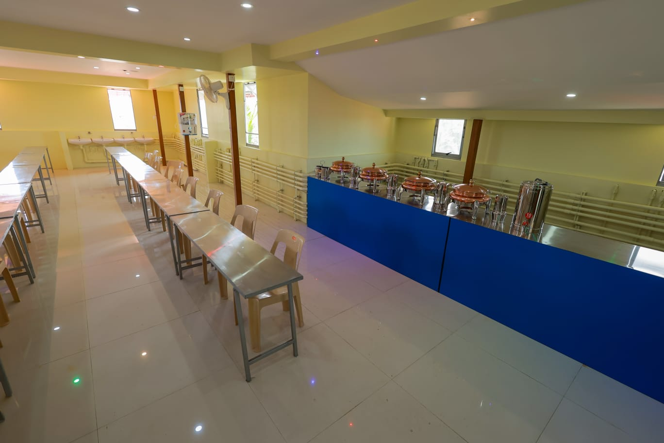 Spacious dining hall with long steel tables, chairs and a buffet counter